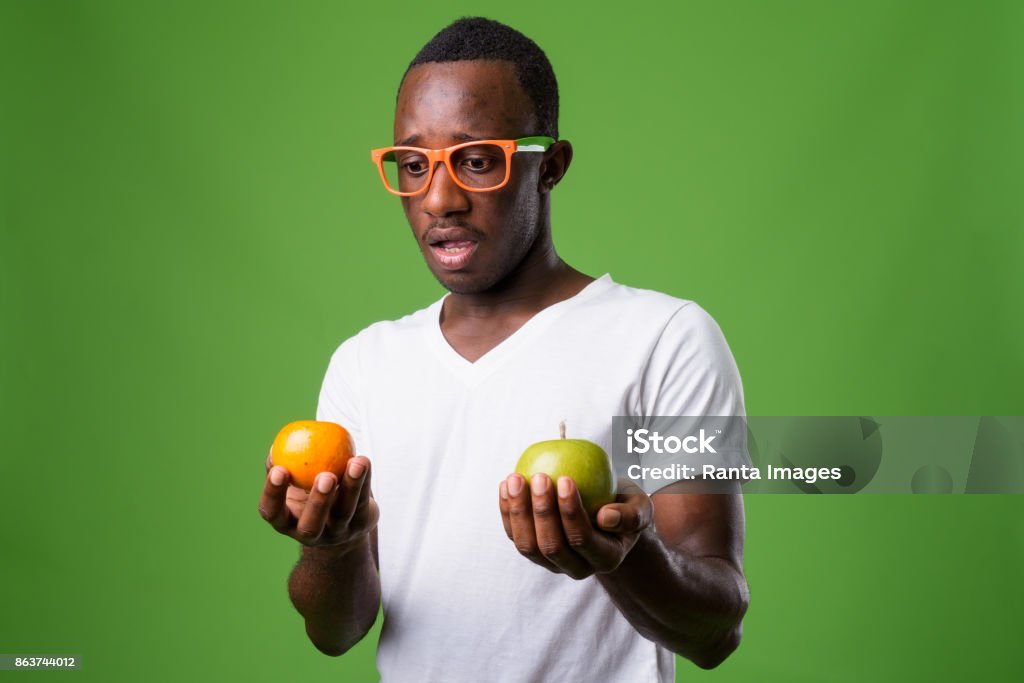 Studio shot of young African man wearing white shirt against green background Studio shot of young African man wearing white shirt against green background horizontal shot Orange - Fruit Stock Photo