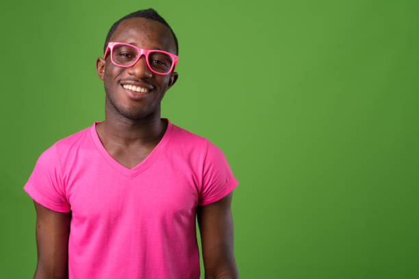 scatto in studio di un giovane africano che indossa una camicia rosa abbinata a occhiali rosa su sfondo verde - occhiali giocattolo foto e immagini stock