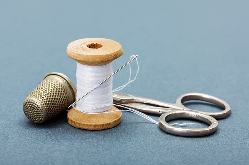 Sewing thread, needle, thimble and scissors on gray background