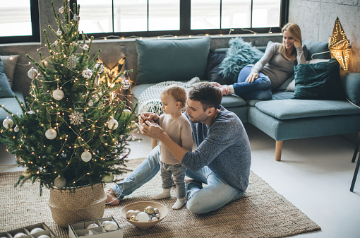 Family with one child decorating Christmas tree. They are happy and enjoy in preparation for holidays.