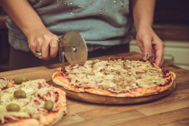 Close up of woman cutting pizza in the kitchen.