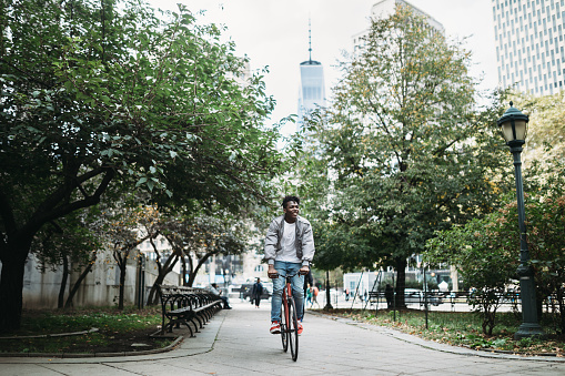 A young African American man explores New York City with his fixed gear bicycle.  One World Trade Center visible in skyline behind him.