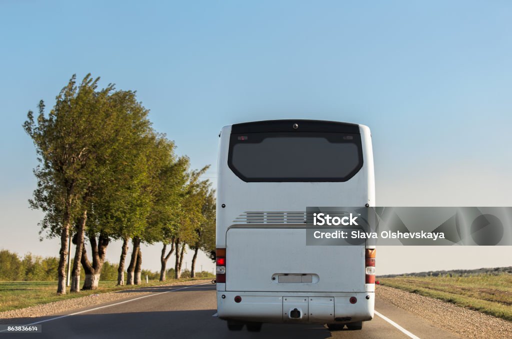White intercity bus is driving along the road. White intercity bus is driving along the road. Back view. Sunny day. The sky without clouds. Bus Stock Photo