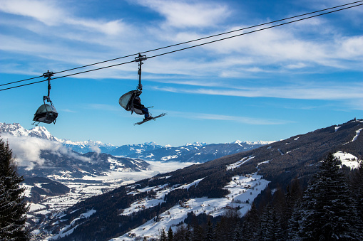 Chairlift travelling across blue alpine sky with mountain range in the background