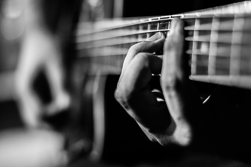 Black and white close up of senior man’s hand with fingers on the neck of an acoustic 12 string guitar.