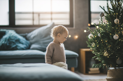 Little child in room with decorated tree, it is Christmas time and  she can't wait to open gifts