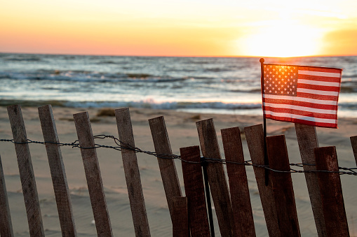 sunset glow illuminating American flag on beach fence