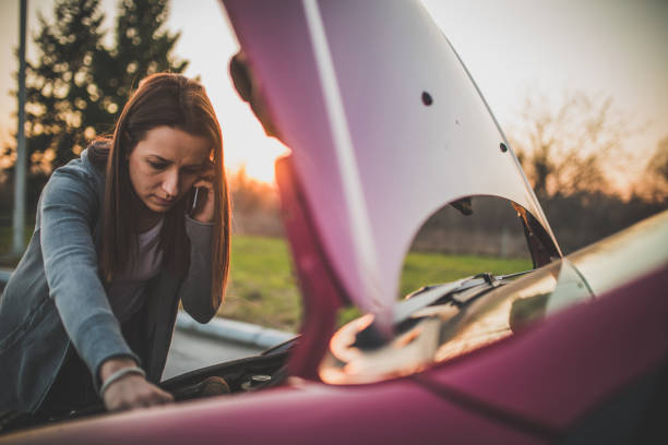Calling Emergency Service Young woman standing by her broken car on the road and using phone to call for help vehicle breakdown stock pictures, royalty-free photos & images