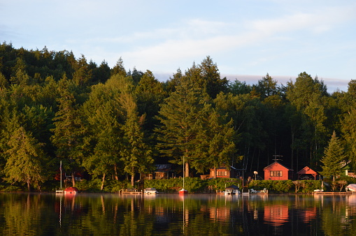 Cabin coastline on Saranac Lake bathed in the morning sunrise. The colored cabins are reflected in the water.
