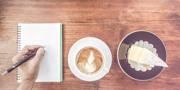 Man, Hand holding cup of coffee,With notebook and pen on wooden table.Copy space for text