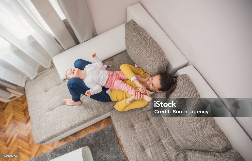 Mother tickling daughter Mother tickling daughter on a sofa in the living room Baby - Human Age Stock Photo