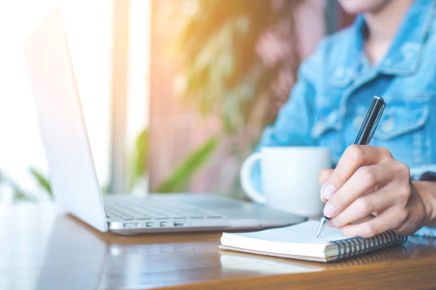 istock Woman hand working on a notebook computer and writing on a notepad with a pen in the office. 864029774