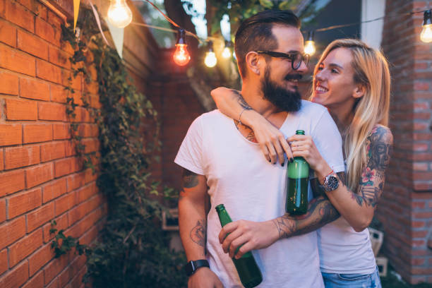 Tattooed Couple Having Fun At Barbecue In Backyard. Looking face to face and embracing.