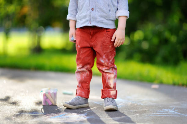 istock Happy little kid boy sitting and drawing with colored chalk on asphalt 864104384