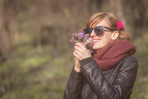 Cute young girl smelling nice bouquet of flowers in nature.