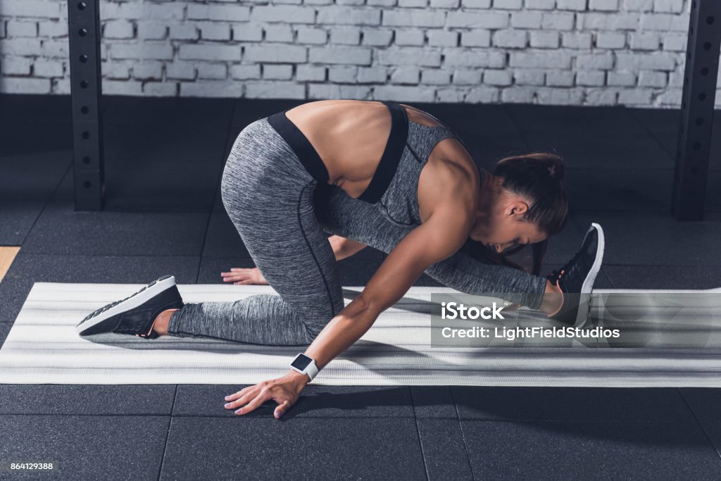 woman stretching on mat side view of young sportive woman stretching on mat before training in gym Active Lifestyle Stock Photo