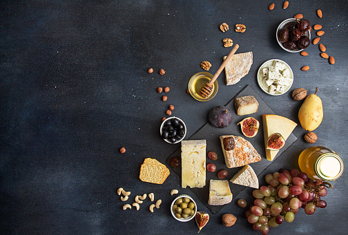Food background with cheese. Blocks of moldy cheese, grapes, figs, honey, pear, dates, pickled prunes, nuts over on dark background. Copy space. Top view