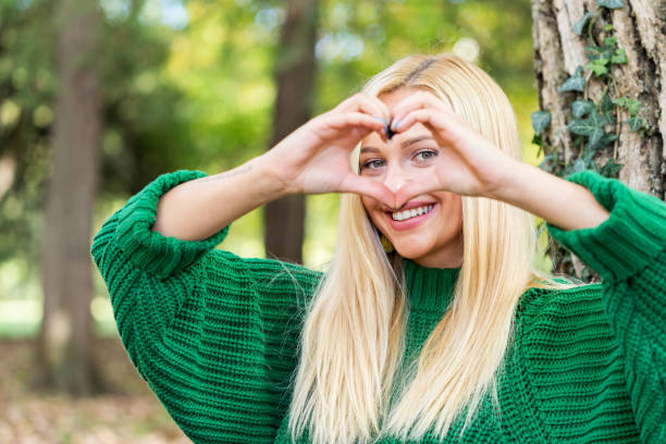 Young woman makes heart shape finger frame in park