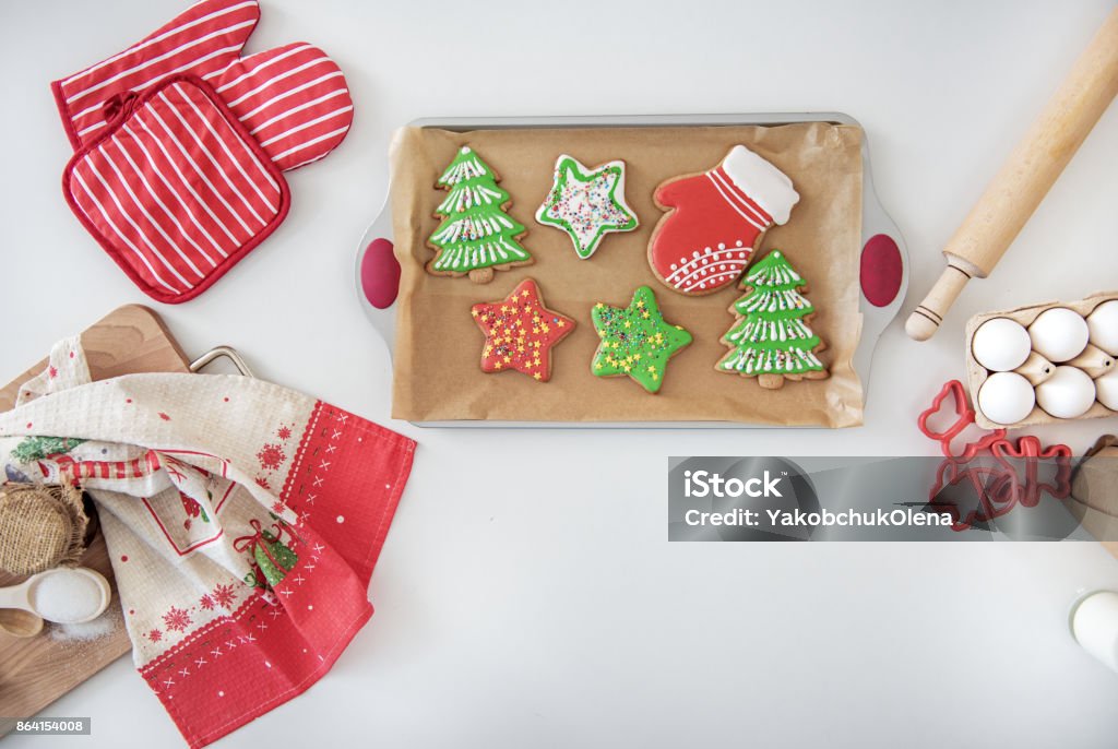 Bright sweet holiday pastry on desk in kitchen Top view close up of delicious colorful Christmas cookies in different shapes on tray. Eggs, rolling pin and red cloth on table Baked Stock Photo