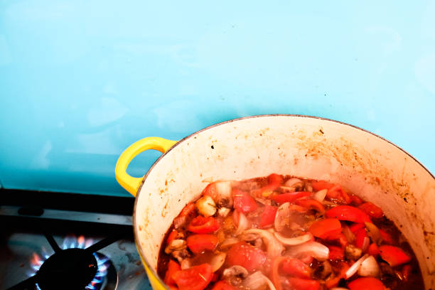 Looking down at a pan containing a tomato-based sauce, simmering away on a gas stove. Cropped view with copy space.