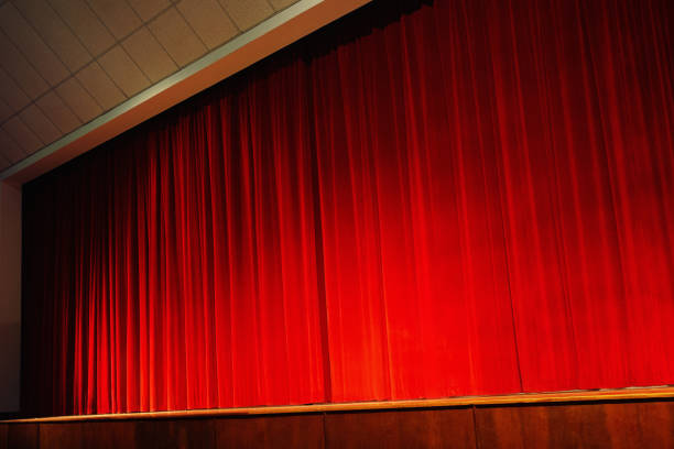 istock Closed red velvet stage curtains, lit by footlights 864158126