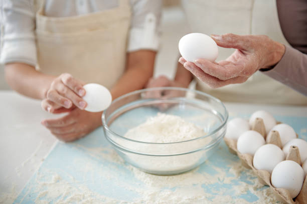 grand-mère et enfant préparant la pâte ensemble - break eggs domestic kitchen breaking photos et images de collection