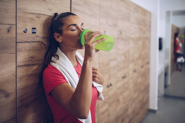 疲れ果てた女性スポーツ トレーニング後のロッカー ルームで水を飲みます。 - refreshing drink ストックフォトと画像