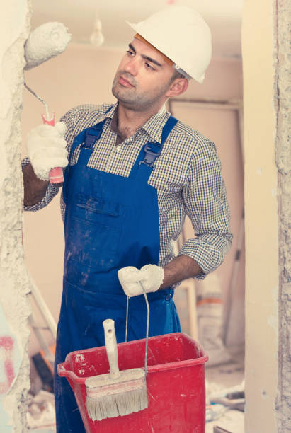istock Builder man in helmet repairing with roller and bucket 864165394
