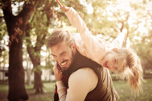 Cheerful father holding his daughter on shoulders and playing together