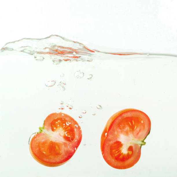 istock cut tomato falls into the water, splashes on white background, close-up 864181762