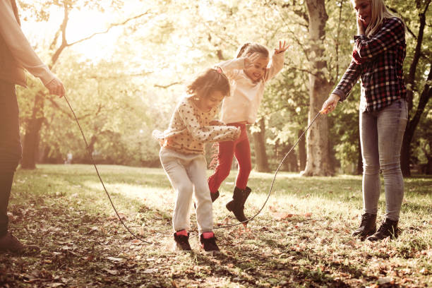 Cheerful family playing with jump rope together in park. stock photo