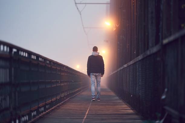 Lonely man on the old bridge Gloomy weather. Lonely man is walking on the old bridge in mysterious fog. walking loneliness one person journey stock pictures, royalty-free photos & images
