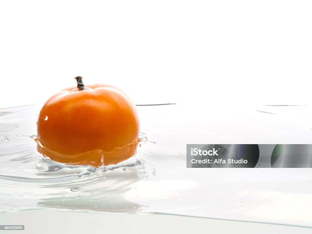 Yellow tomato fall in water. Photo in action. Drops of water. Isolated white background Whole, yellow and ripe tomato falls into the water. Water splashes. Isolated picture on white background Close-up Stock Photo