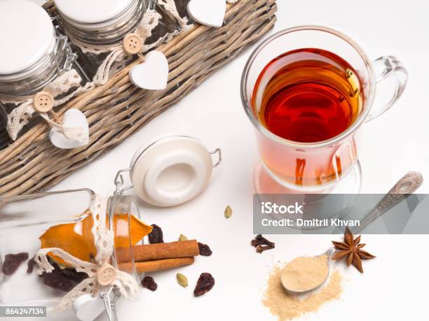 Tea With Spices In A Glass Mug On A White Background Next Basket With Jars And Spices Cinnamon Cardamom Orange Cloves Spoon With Ginger Stock Photo - Download Image Now