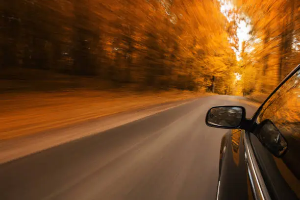 Close up of a sport car speeding on the empty, autumn road with copy space
