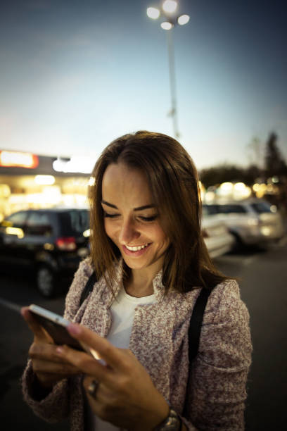 istock Smiling young woman using smart phone on streets by night 864252176