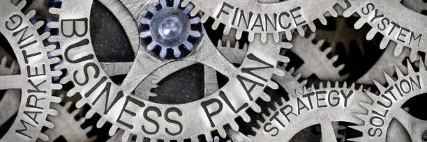 Macro photo of tooth wheel mechanism with BUSINESS PLAN, STRATEGY, FINANCE, SOLUTION, MARKETING, and SYSTEM words imprinted on metal surface