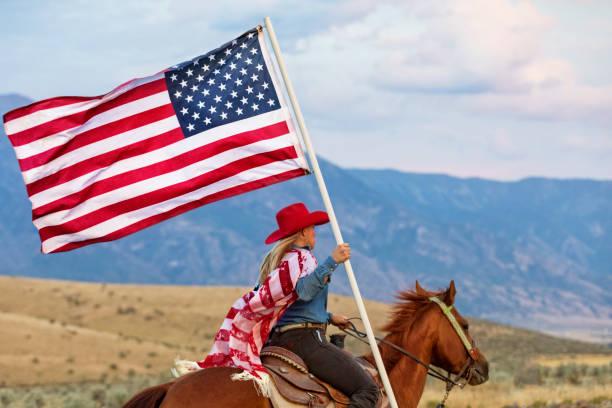 Cowgirl rides her horse over an open range while carrying the American Flag stock photo
