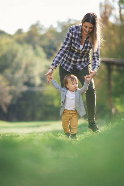 madre che aiuta il suo bambino a camminare - baby first steps autumn child foto e immagini stock