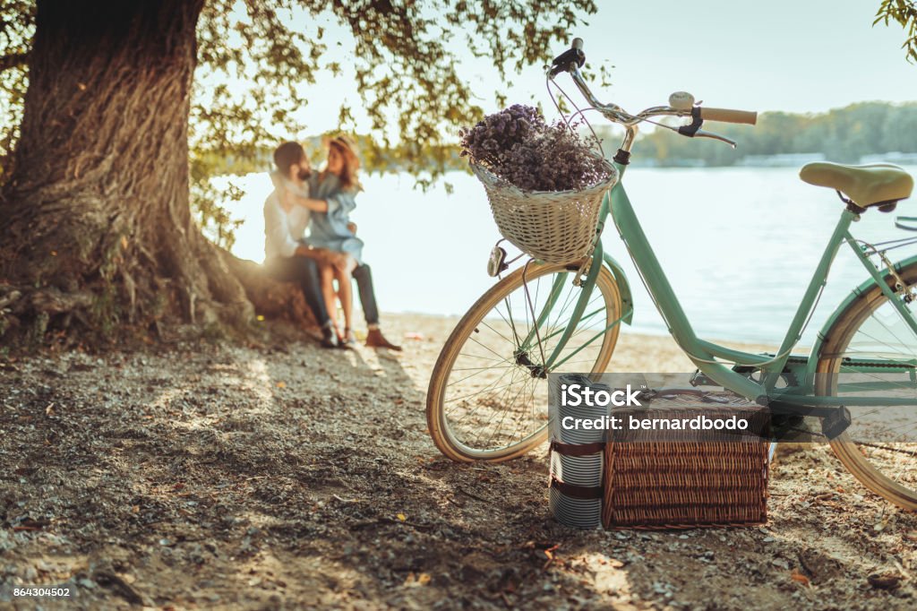 A spontaneous picnic for two A pastel colored bicycle with a basket full of picnic goodies and a cute couple cuddling under a tree. Picnic Stock Photo