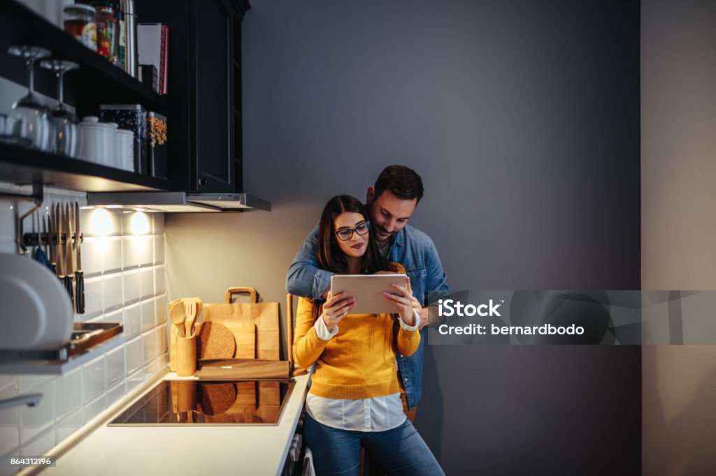 What do you feel like ordering? A young couple using their tablet in the kitchen to order some food. Couple - Relationship Stock Photo