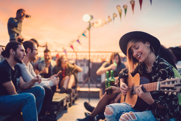 Friends drinking and partying on the rooftop Group of friends enjoying a social gathering with guitar music on the rooftop building terrace photos stock pictures, royalty-free photos & images