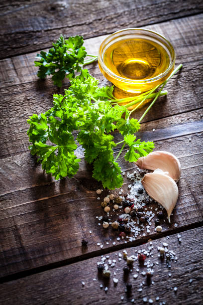 Top view of fresh organic parsley bunch shot on rustic wooden table. Some salt and peppercorns are beside the leaves as well as two garlic cloves and a small glass bowl filled with olive oil. Copy space available for text and/or logo. Predominant colors are green and brown. DSRL studio photo taken with Canon EOS 5D Mk II and Canon EF 100mm f/2.8L Macro IS USM