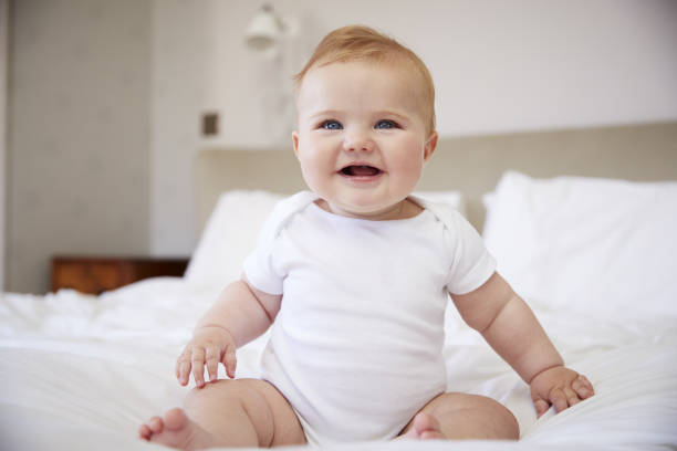 Happy Baby Boy Sitting On Parents Bed Happy Baby Boy Sitting On Parents Bed babygro stock pictures, royalty-free photos & images