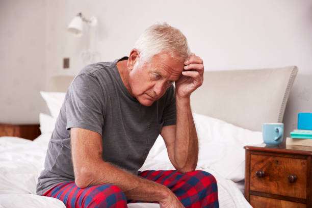 Senior Man Sitting On Bed At Home Suffering From Depression Senior Man Sitting On Bed At Home Suffering From Depression old man pajamas photos stock pictures, royalty-free photos & images