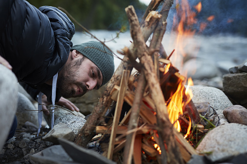 Springtime in mountains. Couple sitting by the fire. River in the background