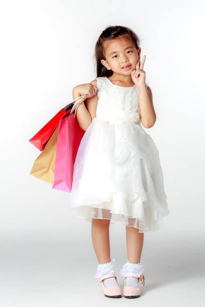 ショッピング バッグ立っていると白い背景にポーズとドレスのかわいいアジア女の子 - paying children only retail childhood ストックフォトと画像