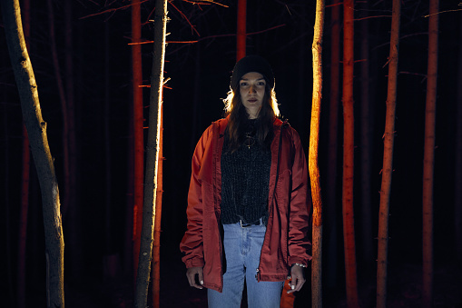 Young woman standing between tree trunks. Dark and spooky forest