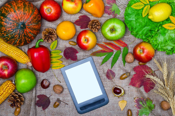 istock Autumn background: pumpkin, yellow leaves, apples and tablet on the table, top view. 864384810
