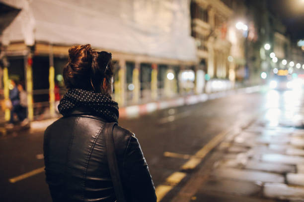 Young woman walking alone on the streets of London at night Young woman walking on the streets of London alone, wearing a black leather jacket and a backpack. walking loneliness one person journey stock pictures, royalty-free photos & images